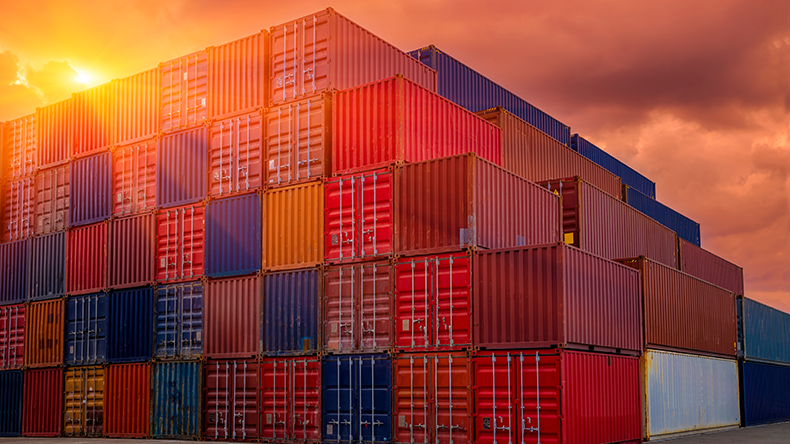 Shipping containers being unloaded at port facilities at sunset