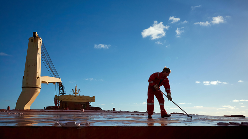 Ships crew members painting hatch cover outdoors with bright blue sky on a background