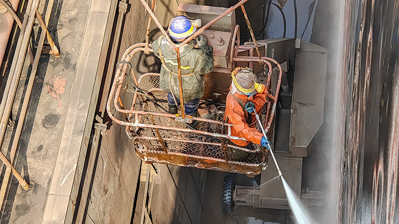 Shipyard labours using hydroblast gun to remove marine growth on ship side