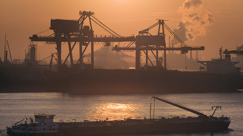 Sunset at Port of Rotterdam with cranes, a large bulk carrier and a passing river cargo ship, the Netherlands.  EschCollection / Getty Images