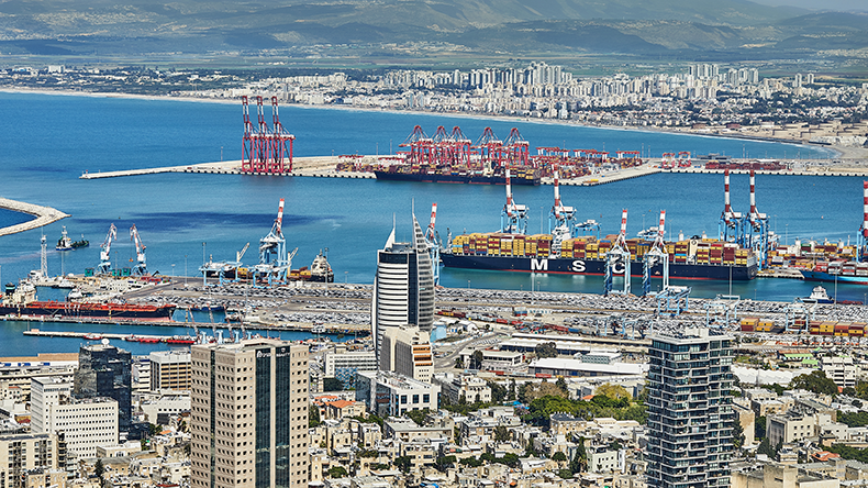 Numerous cargo ships anchored off the coast of Haifa, Israel under a calm blue sky