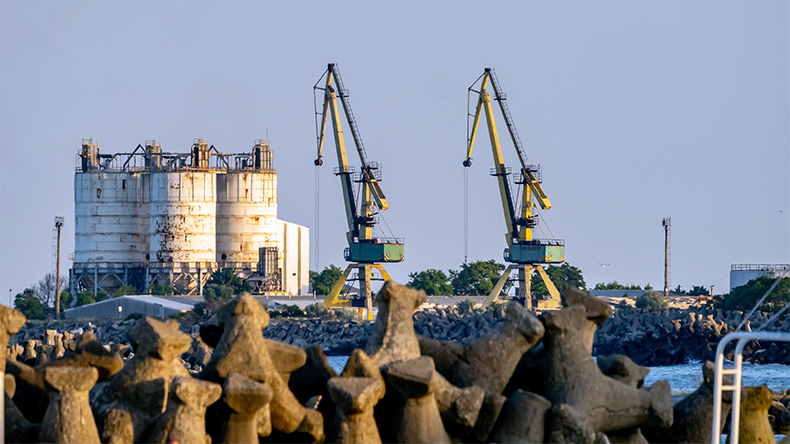 Industrial harbor cranes and silos behind Black Sea tetrapod barrier