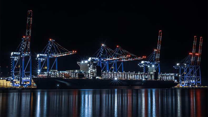 Gdansk port with a containership being loaded at night with lights reflecting in water