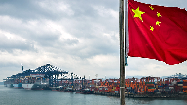  Chinese national flag is seen in the foreground with containerships, cranes and stacked shipping containers at the Yantian International Container Terminal under cloudy skies