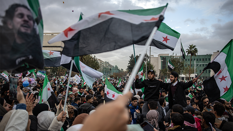 People wave flags as they celebrate the first anniversary of the overthrow of the Assad regime in Umayyad Square on December 8, 2025 in Damascus, Syria