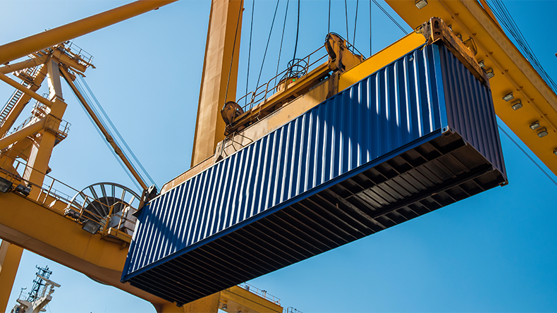 Container being lifted by a gantry crane against a blue sky