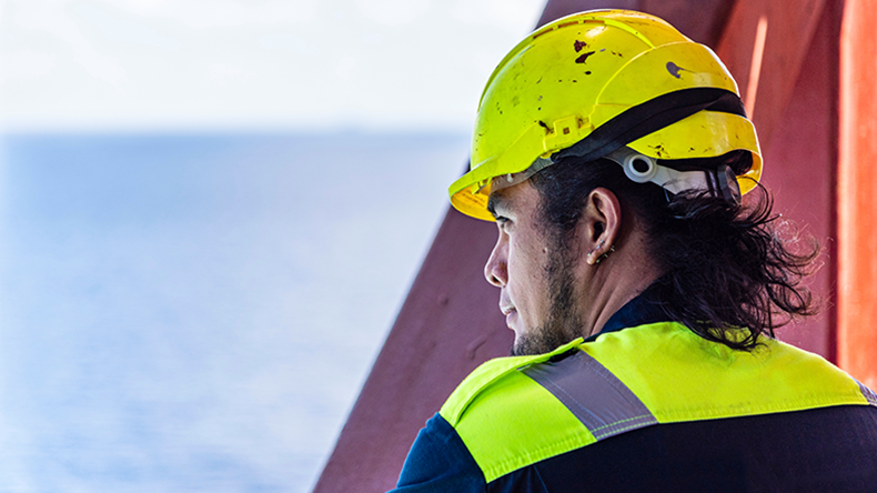 Portrait of a young Filipino officer in protective clothing and a yellow helmet, standing aboard a containership