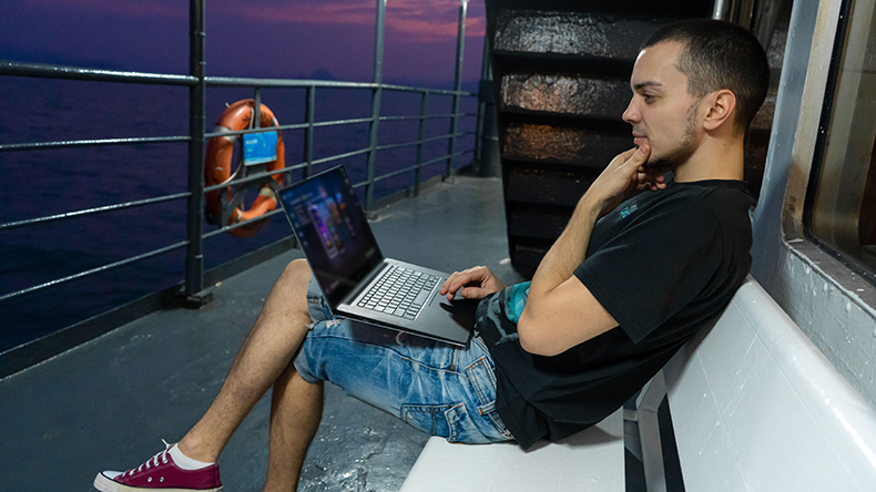  A young man works on a laptop on the deck of a ship