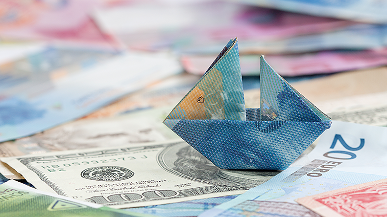 An image of a ship made of a folded banknote on a sea of money in various currencies.