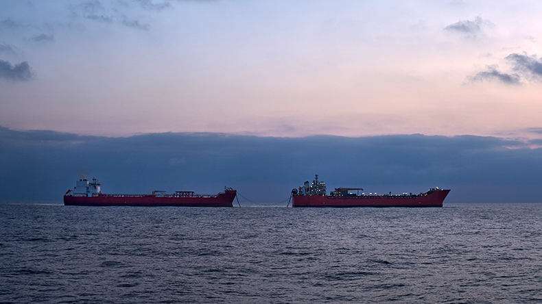 Silhouette of two oil tankers in the sea, early in the morning, with blue sky and calm water