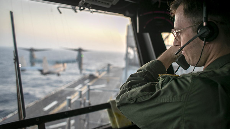 A naval officer aboard USS Tripoli (LHA 7) oversees flight operations from the control tower as the amphibious assault ship sails in the Arabian Sea