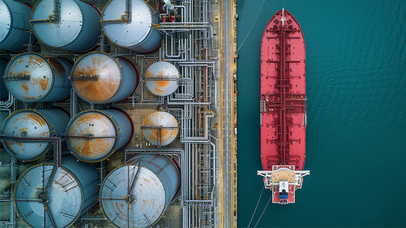 Aerial view of tanker docked next to industrial oil and gas tank storage complex 